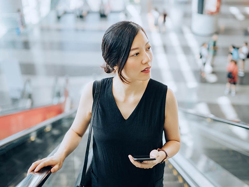 A woman holding mobile while standing in Escalator